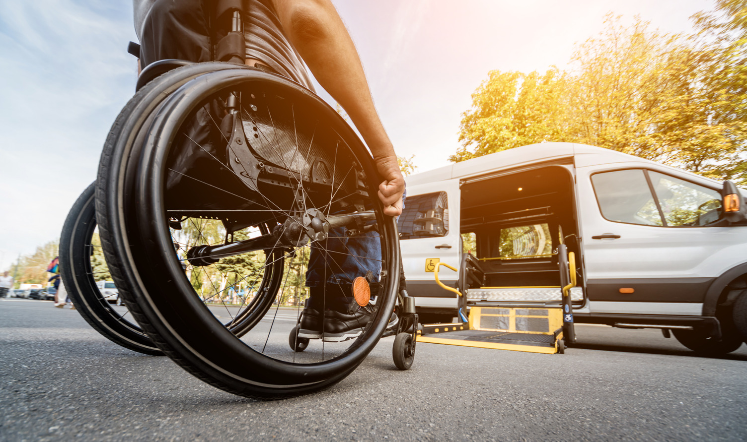 A person in a wheelchair moves towards a wheelchair lift on a specialized transit vehicle parked outside during the day.