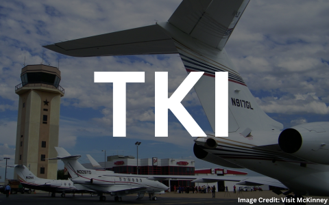 A tail of a jet aircraft with the Air Traffic Control tower in the background at McKinney National Airport