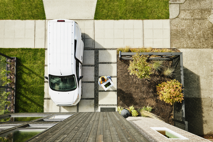 Overhead view of female delivery driver carrying produce box to front door of home